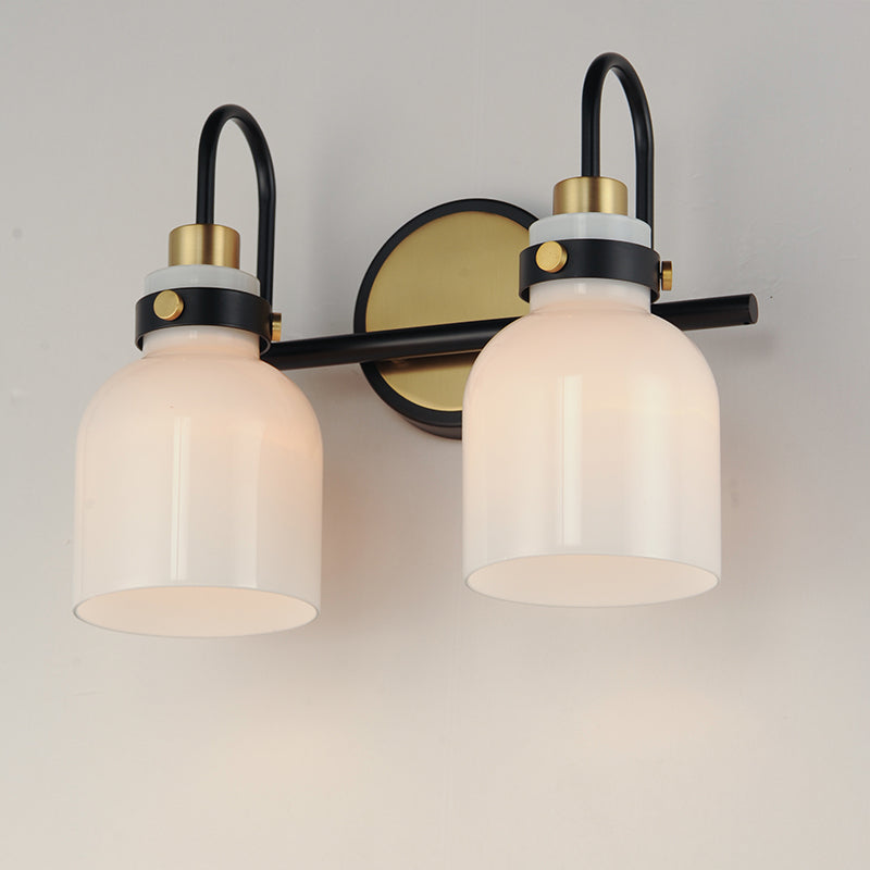 a wall-mounted light fixture with two white glass shades and a black and gold metal frame, turned on